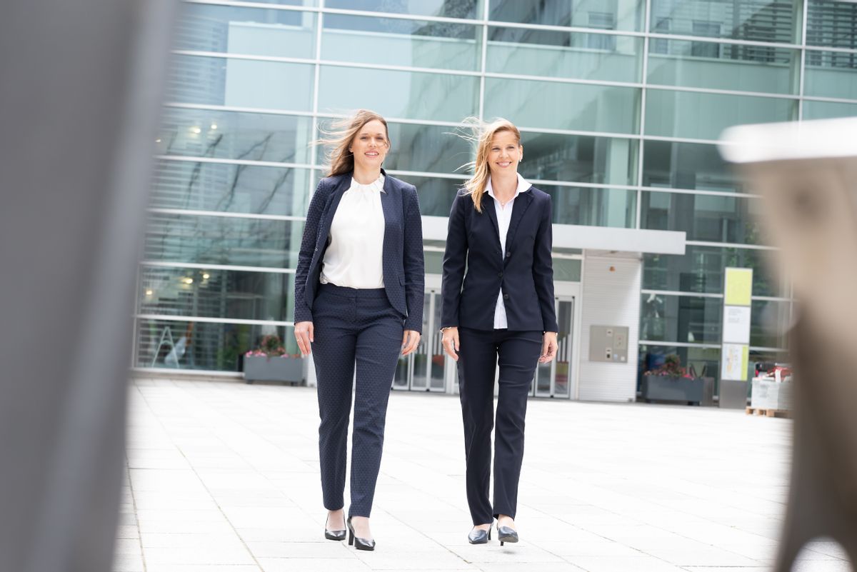 Mag. Nina Engelmayer und Dr. Susanne Chyba gehen vor einem modernen Gebäude der Kamera entgegen.